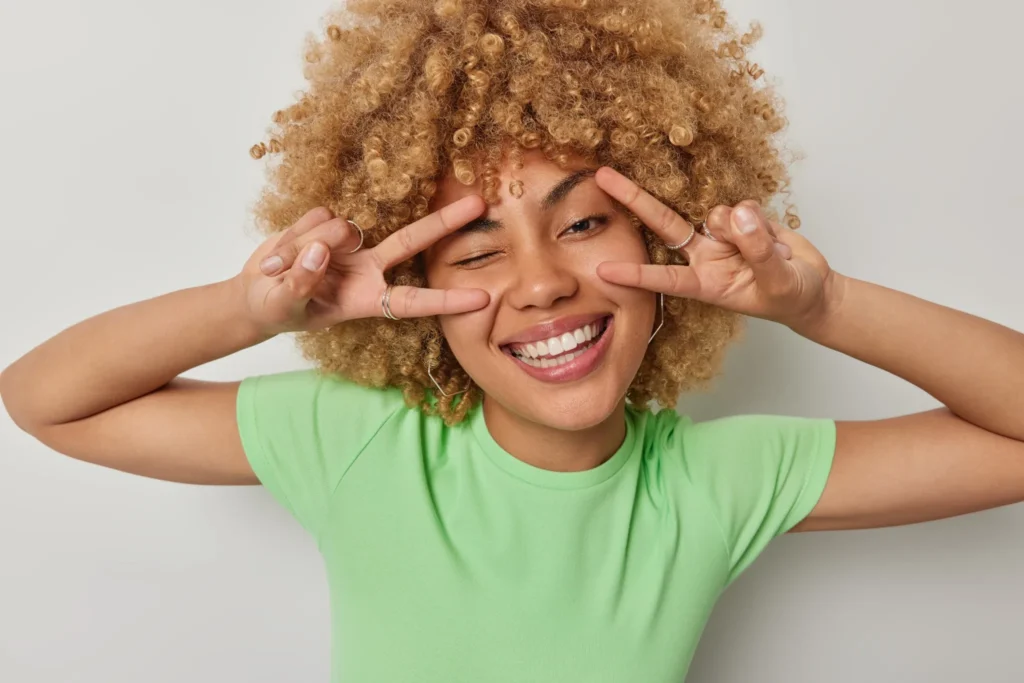 Young woman flashing a bright, carefree smile with a peace gesture – perfect dental care representation