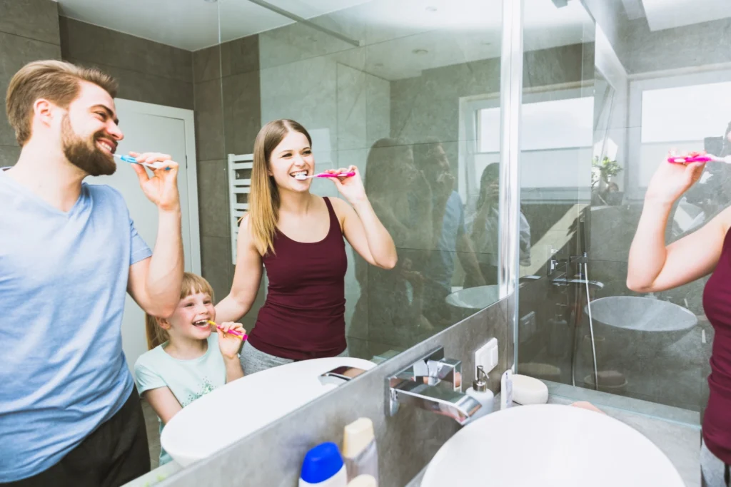 Happy family brushing teeth together in front of a mirror to promote daily oral care